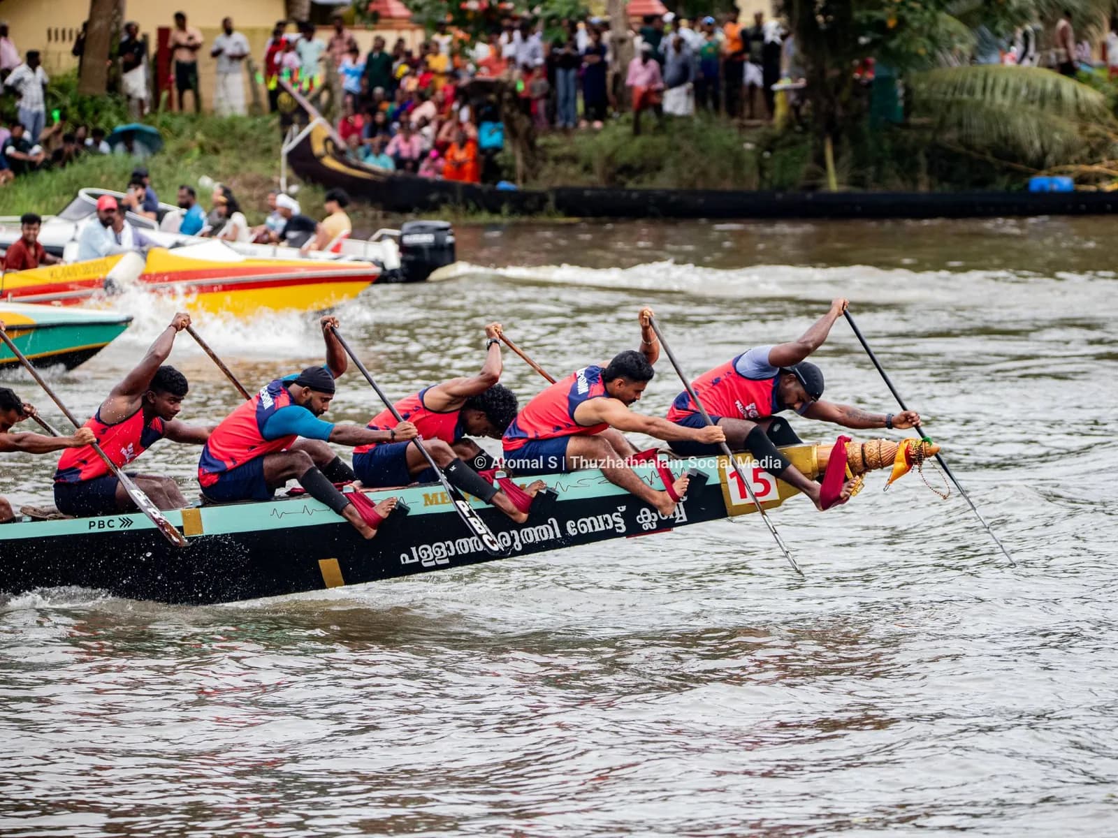 Snake boat crew in red pulling hard at a Kerala boat race, crowds lining the bank